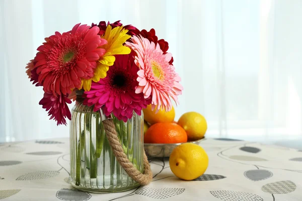 Kleurrijke gerbera's in glazen vaas met fruit op tafel op gordijnen achtergrond — Stockfoto