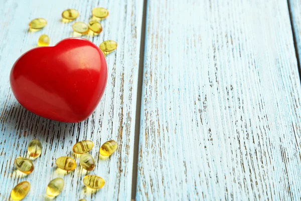 Red heart and cod liver oil on blue wooden background — Stock Photo, Image