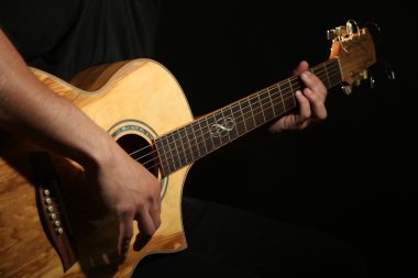 Genç adam akustik gitarla karanlık arka planda çalıyor.