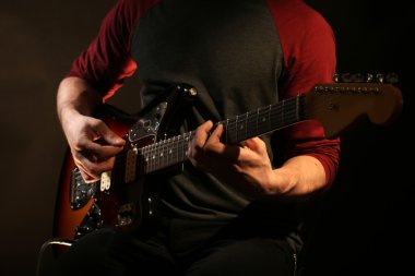 genç adam elektro gitar koyu arka plan üzerinde oynamak