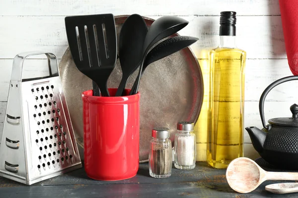 Utensilios de cocina de plástico en taza roja con botella de aceite de oliva sobre fondo de madera —  Fotos de Stock