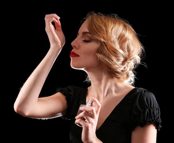 Hermosa joven con botella de perfume sobre fondo negro — Foto de Stock