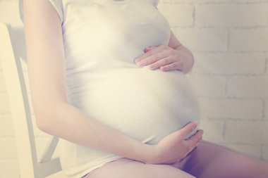 Açık renkli sandalye üzerinde oturan genç hamile kadın