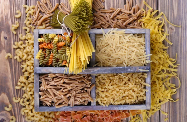 Diversi tipi di pasta in scatola su sfondo di legno — Foto Stock