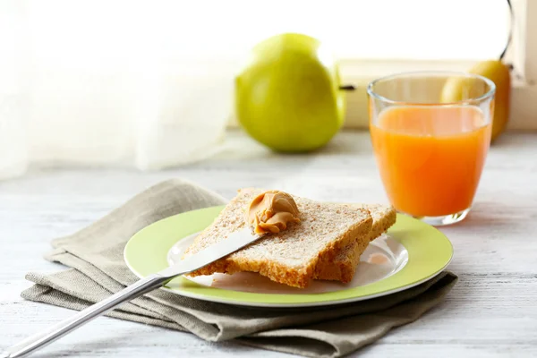 Toasts with peanut butter on plate with cup of tea and juice on light background — Stock Photo, Image