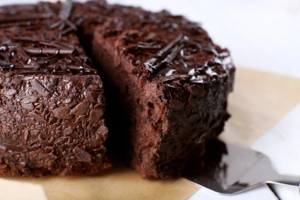 Bolo de chocolate saboroso fatiado em folha de pergaminho na mesa de madeira, close-up — Fotografia de Stock