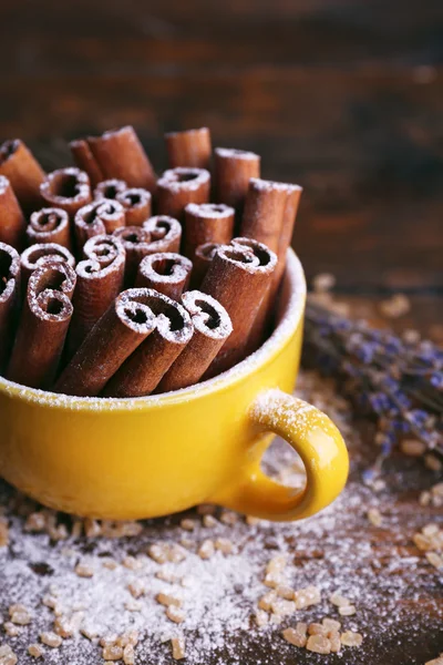 Varas de canela na xícara com açúcar e lavanda no fundo da mesa de madeira — Fotografia de Stock