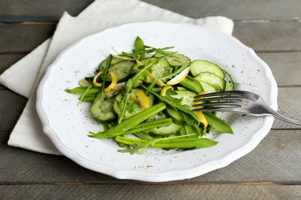 Green salad with cucumber, arugula and lemon peel on wooden table, closeup — Stock Photo, Image