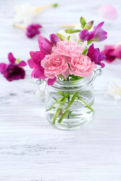 Beautiful spring flowers in glass bottle on wooden background — Stock Photo, Image