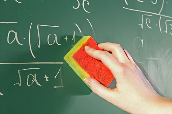 Teacher hand wiping off formulas on blackboard background — Stock Photo, Image