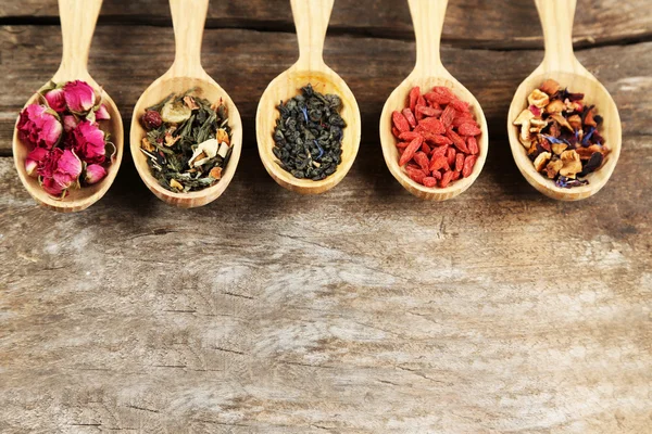 Collection of tea and natural additives in wooden spoons, on old wooden table — Stock Photo, Image