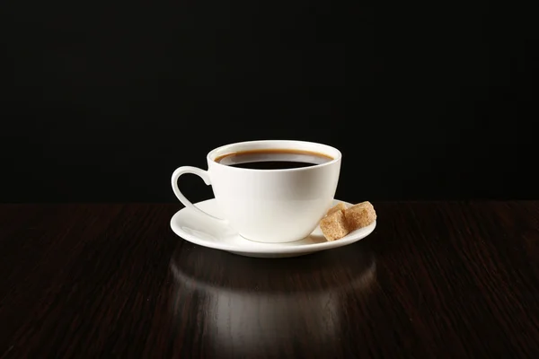 Šálek kávy s kusový cukr na dřevěný stůl, na tmavém pozadí — Stock fotografie