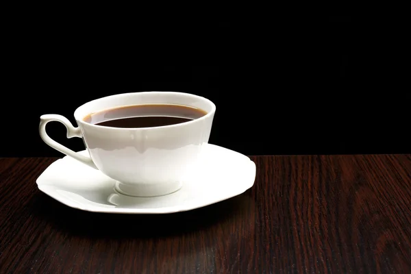 Чашка кави на дерев'яному столі, на темному фоні — стокове фото