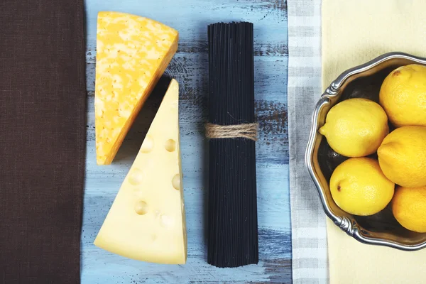 Queso, espaguetis negros y limones en vista de mesa de madera — Foto de Stock