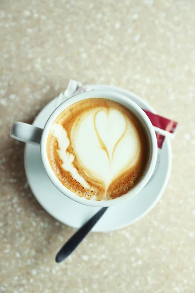 Cup of cappuccino with heart on foam on table in cafe — Stock Photo, Image