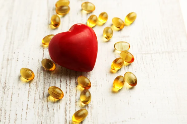 Red heart and cod liver oil, on wooden background — Stock Photo, Image