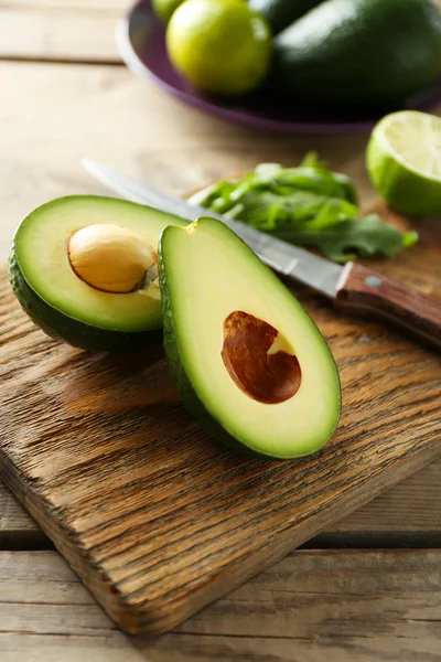 Avocado affettato e lime limone sul tagliere, su fondo di legno — Foto Stock