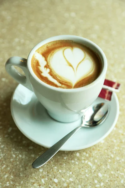 Cup of cappuccino with heart on foam on table in cafe Royalty Free Stock Photos