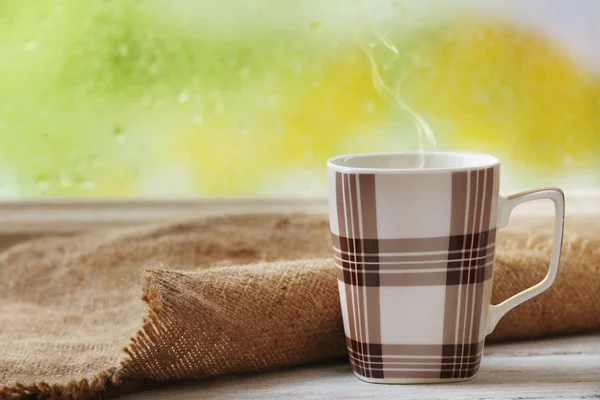 Tasse Heißgetränk mit Sacktuch auf Fensterbank auf Regen Hintergrund — Stockfoto