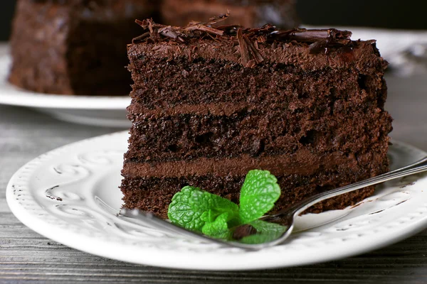 Delicious chocolate cake in white plate with mint on wooden table background, closeup — Stock Photo, Image