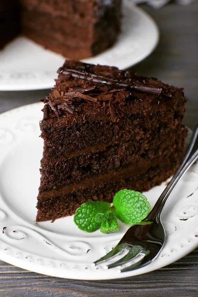 Вкусный шоколадный торт в белой тарелке с мятой на деревянном фоне стола, крупным планом — стоковое фото