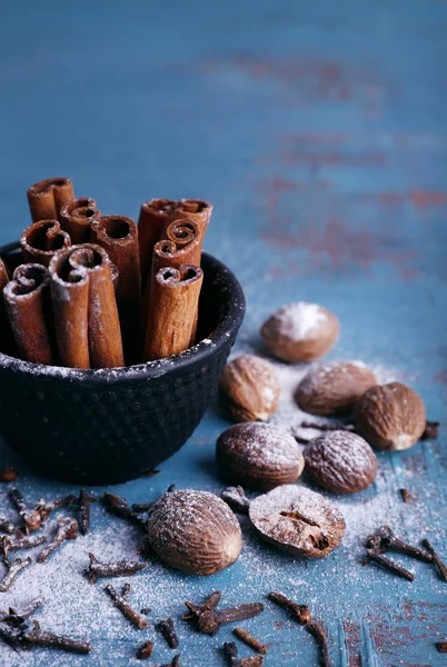 Bastoncini di cannella in ciotola, noce moscata e chiodi di garofano su sfondo tavolo di legno colore — Foto Stock