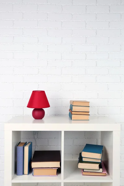 Houten plank met boeken en lamp op bakstenen muur achtergrond — Stockfoto