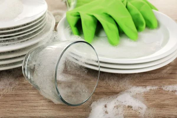Посуда в пене с перчатками на столе крупным планом — стоковое фото
