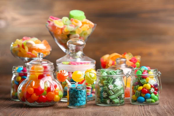 Colorful candies in jars on table on wooden background — Stock Photo, Image