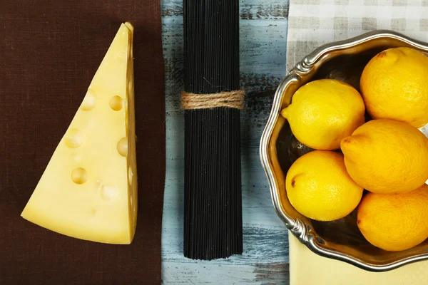 Queso, espaguetis negros y limones en vista de mesa de madera —  Fotos de Stock