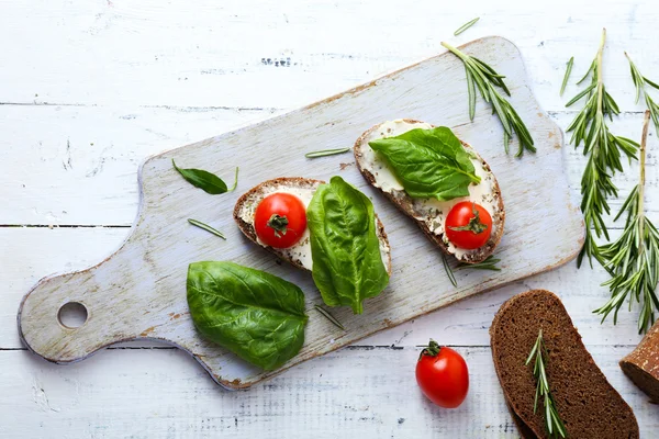 Läckra smörgåsar med tomater och greener på skärbräda på bordet på nära håll — Stockfoto