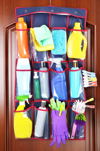 Household chemicals in holder hanging on wooden door background — Stock Photo, Image