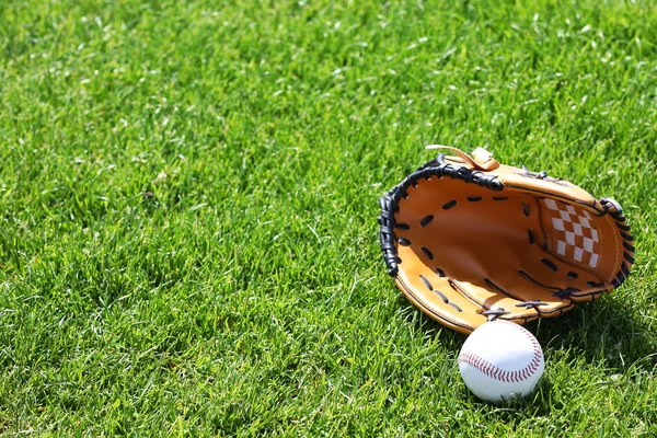 Baseball ball and glove on green field — Stock Photo, Image