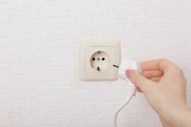 Hand putting plug in electricity socket close up clipart