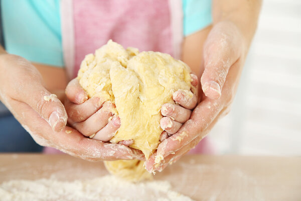 Little girl preparing cookies with mother in kitchen, close-up