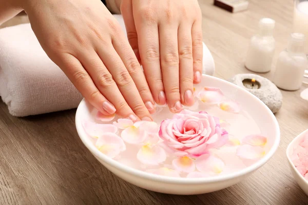 Manos femeninas y tazón de agua de spa con flores, primer plano — Foto de Stock