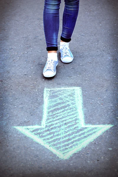 Kvinnliga fötter och ritade pil på trottoaren bakgrund — Stockfoto