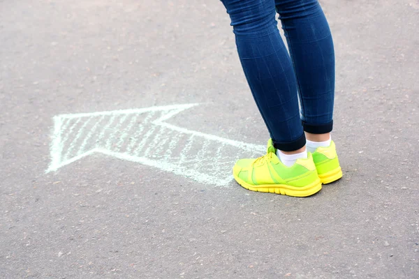 Женские ноги и рисунок стрелки на фоне тротуара — стоковое фото