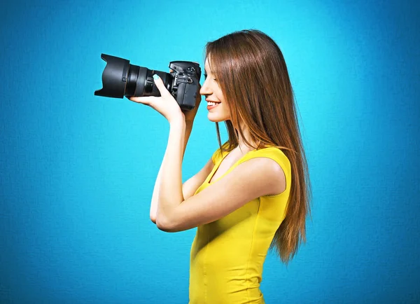 Ung kvinnlig fotograf tar bilder på blå bakgrund — Stockfoto