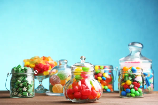 Tégelyek az asztalon a kék háttér színes cukorkák — Stock Fotó