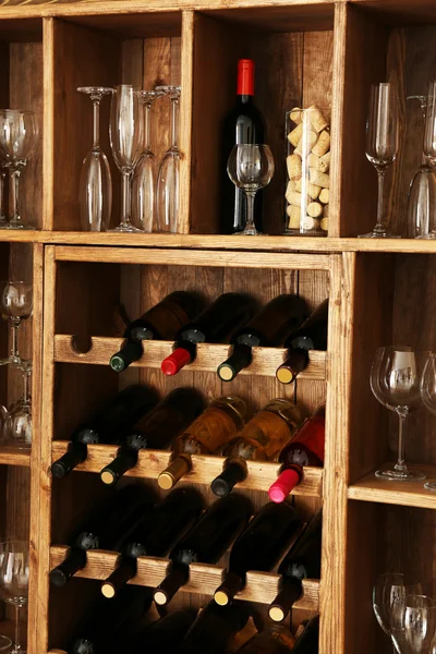 Estanterías con botellas de vino con copas sobre fondo de pared de madera — Foto de Stock