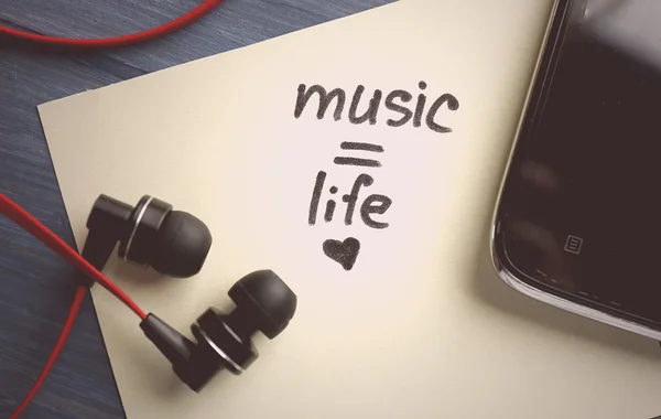 Earphones with text Music - life on sticker on wooden table, closeup — Stock Photo, Image