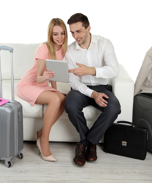 Portrét mladého šťastnému páru s zavazadla, digitální tabletu a laptop sedí na pohovce. Izolované na bílém — Stock fotografie