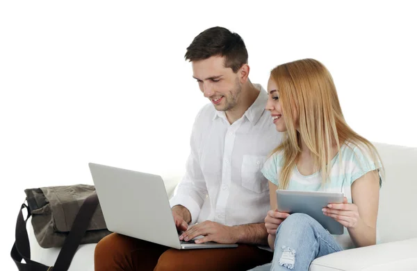 Retrato de pareja feliz joven con equipaje, tableta digital y portátil sentado en el sofá. Aislado sobre blanco — Foto de Stock