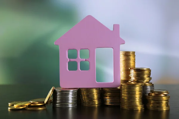 Modelo de casa com moedas na mesa de madeira no fundo borrado — Fotografia de Stock