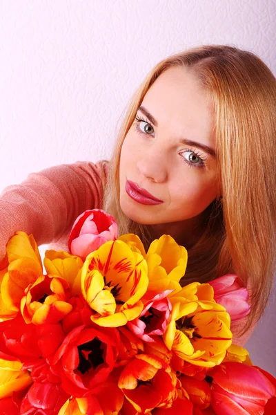 Portrait of young woman with beautiful bouquet of tulips on wallpaper background — Stock Photo, Image