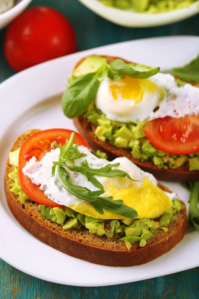 Sanduíches saborosos com ovo, abacate e legumes no prato, no fundo de madeira — Fotografia de Stock