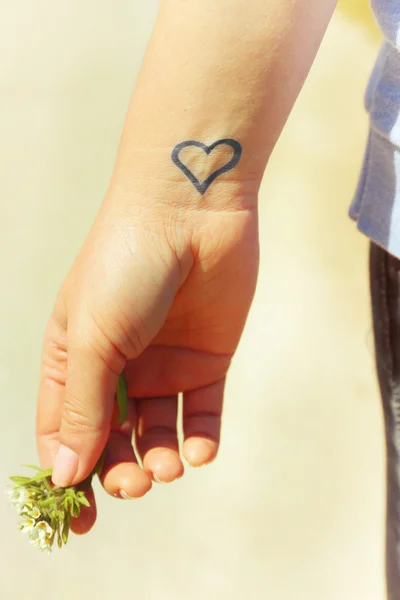 Cerca de la muñeca de la joven con el corazón tatuado en ella, sobre el fondo de la naturaleza — Foto de Stock