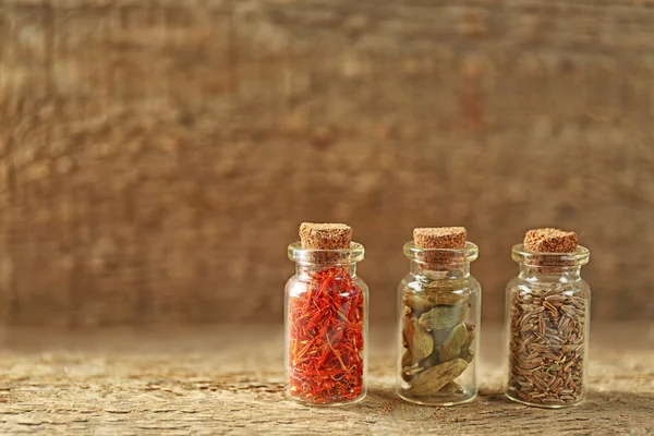 Assortiment van specerijen in glazen flessen op houten achtergrond — Stockfoto