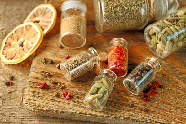 Assortiment d'épices dans des bouteilles en verre sur planche à découper, sur fond en bois — Photo